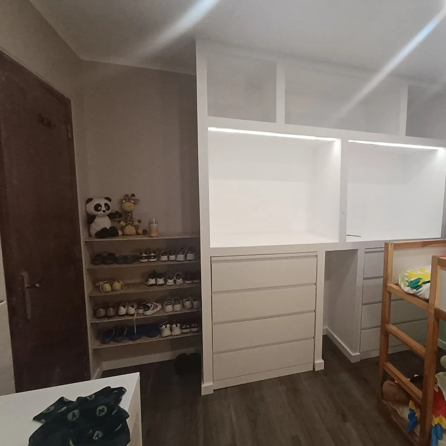 Móvel embutido branco com gavetas, nichos iluminados e sapateira